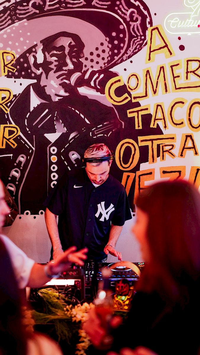A bartender mixes drinks in front of a mural featuring a musician.