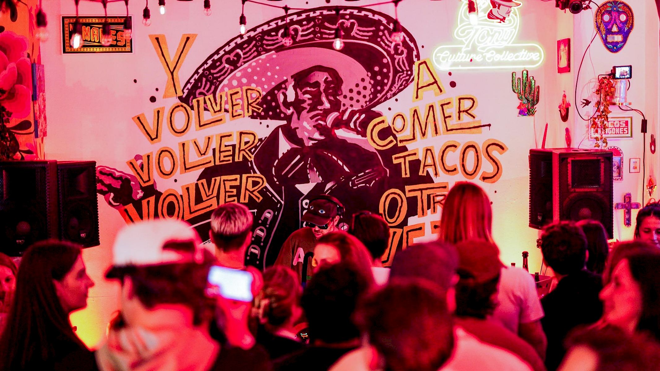 Vibrant bar scene with people in front of a mural featuring a man in a sombrero.