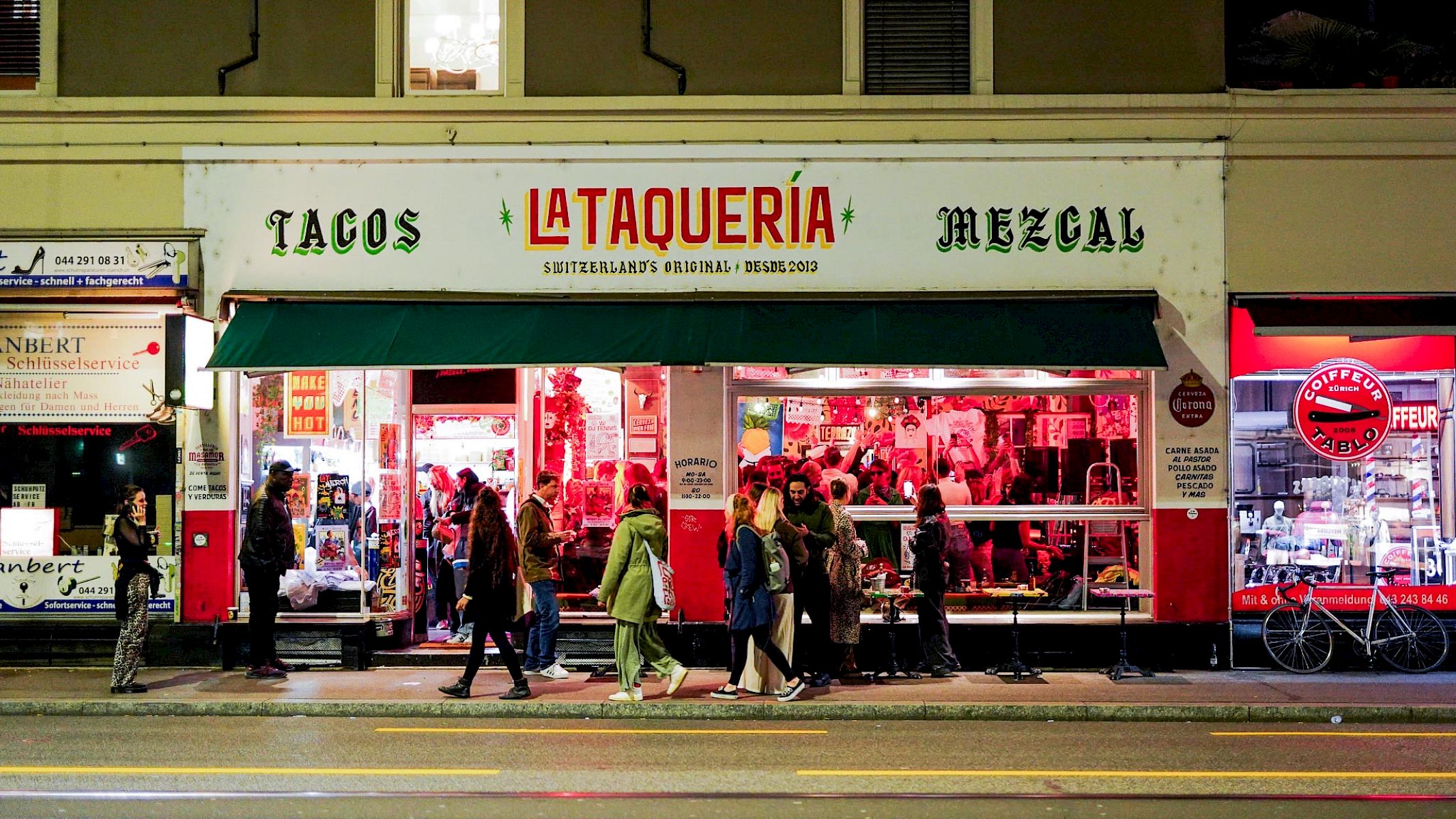A lively restaurant named 'La Taquería' serving tacos and mezcal on a bustling street.