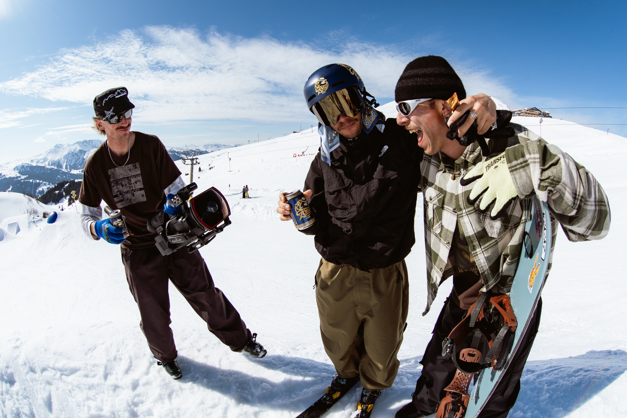 Drei Snowboarder genießen einen El Tony Mate auf der Piste bei sonnigem Wetter.